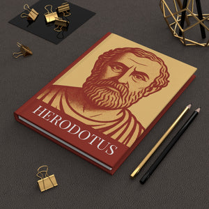 Hardcover journal with a bold orange and yellow illustration of Greek historian Herodotus on a dark flat surface