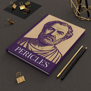 Hardcover journal with Pericles illustration on a dark surface with office supplies.