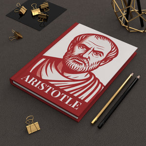 Hardcover journal with Aristotle red and white illustration on a dark surface with office supplies