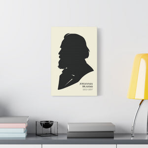 Canvas wall art with a black on ivory silhouette illustration of musician Johannes Brahms on a wall above a desk with books and a lamp.