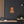 Canvas wall art with a bold illustration of Roman emperor Commodus on a dark wall above a wooden shelf.