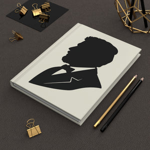 Hardcover journal with a black-on-ivory silhouette illustration of musician Claude Debussy on a dark surface with office supplies.