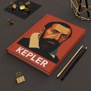 Hardcover journal with a bold illustration of astronomer Johannes Kepler on a dark surface with office supplies