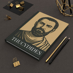 Hardcover journal with a bold black and beige illustration of ancient Greek historian Thucydides lying flat on a dark surface